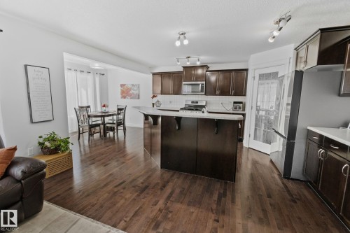 The property features rich hardwood flooring throughout, a kitchen with dark cabinetry, stainless steel appliances, and a central island with a light-colored countertop - 1115 61 Street, Edmonton, AB - Indoor Photo Showing Kitchen