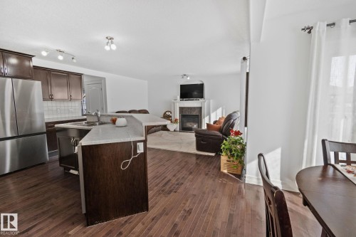 This bright interior features hardwood floors throughout, a kitchen with stainless steel appliances and dark wood cabinetry, and a living area with a fireplace - 1115 61 Street, Edmonton, AB - Indoor Photo Showing Other Room With Fireplace