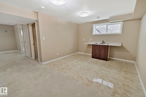 The property features a versatile area with a window, a sink with a dark wood cabinet, and a combination of carpet and tiled flooring - 1115 61 Street, Edmonton, AB - Indoor
