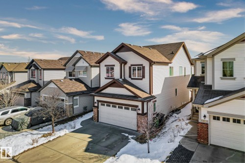 This property features a two-story design with white siding and dark trim, a prominent attached garage with a white door, and a driveway - 1115 61 Street, Edmonton, AB - Outdoor With Facade
