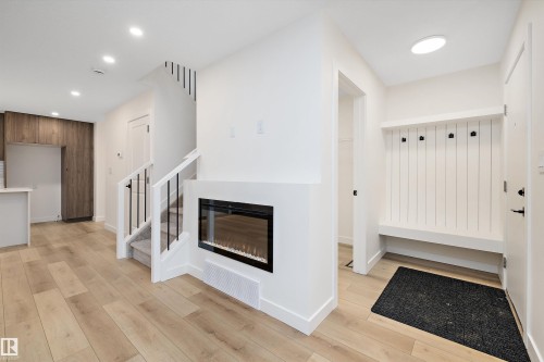 Entryway featuring built-in bench seating with coat hooks, a contemporary electric fireplace, wood-finish flooring, a carpeted staircase with white risers and dark balusters, and recessed ceiling lighting - 11418 96 Street, Edmonton, AB - Indoor With Fireplace