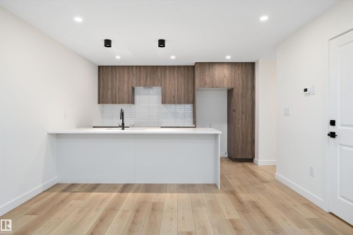 Modern kitchen featuring white countertops, wood-finish cabinetry, a white subway tile backsplash, and a black matte faucet - 11418 96 Street, Edmonton, AB - Indoor Photo Showing Kitchen