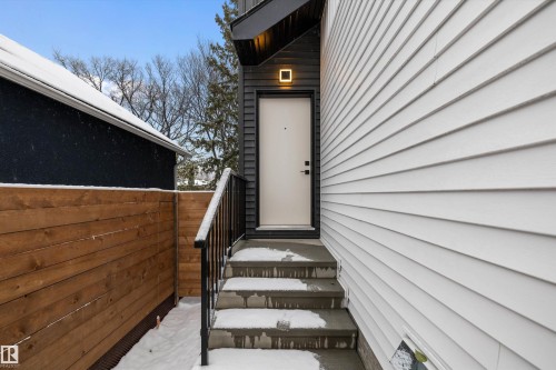 Entryway featuring concrete steps with a black metal handrail, a white door, and a modern exterior light fixture - 11418 96 Street, Edmonton, AB - Outdoor With Exterior