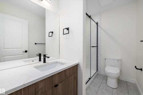 Bathroom featuring a wood-finish vanity with a white countertop and integrated sink, matte black fixtures, a frameless mirror, and a glass-enclosed shower with subway tile surround - 11418 96 Street, Edmonton, AB - Indoor Photo Showing Bathroom