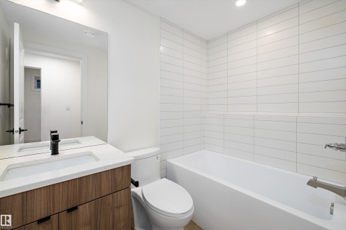Bathroom featuring a wood-finish vanity with a built-in sink, a black matte faucet, and a large wall mirror - 11918 93 Street, Edmonton, AB - Indoor Photo Showing Bathroom