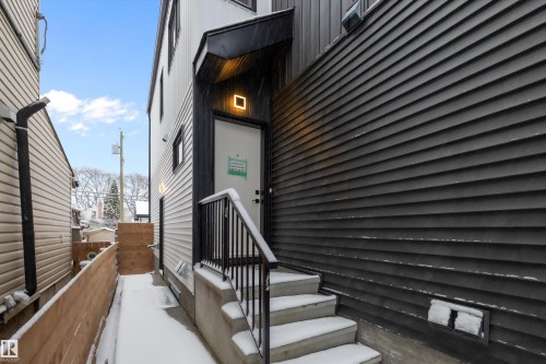 Exterior side entrance featuring a modern square wall light, a black metal handrail, and concrete steps - 11918 93 Street, Edmonton, AB - Outdoor With Exterior
