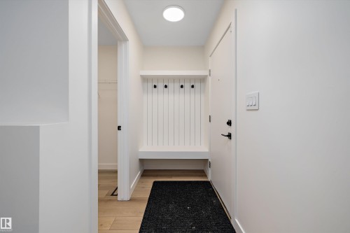 Entryway mudroom bench with integrated coat hooks, showcasing wood-finish flooring, a contemporary flush-mount ceiling light, and a white interior door with matte black hardware - 11918 93 Street, Edmonton, AB - Indoor Photo Showing Other Room