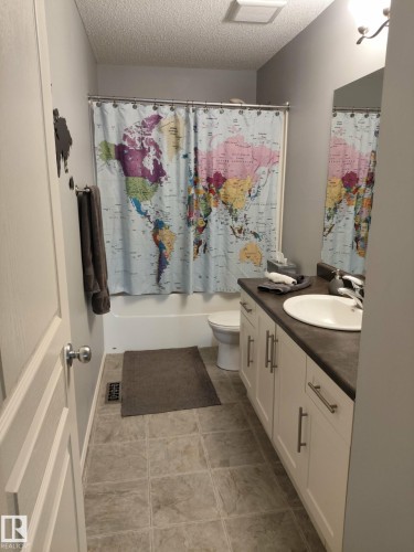 Full bathroom featuring a white vanity with a dark countertop, an integrated sink, and brushed nickel hardware - 59 Rue Monette, Beaumont, AB - Indoor Photo Showing Bathroom