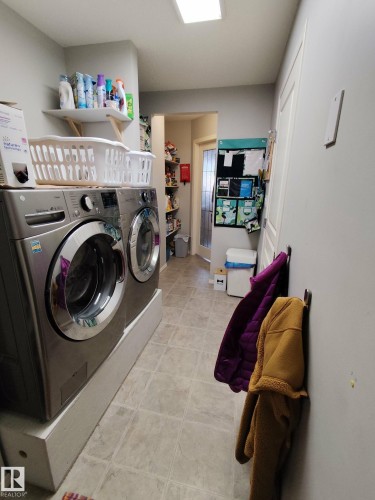 Dedicated laundry area with front-loading appliances on elevated bases, tile-style flooring, a wall-mounted shelf, and recessed lighting - 59 Rue Monette, Beaumont, AB - Indoor Photo Showing Laundry Room