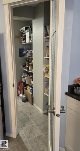Walk-in pantry featuring extensive shelving, tile flooring, and a frosted glass panel door - 59 Rue Monette, Beaumont, AB - Indoor Photo Showing Other Room