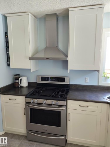 Stainless steel range with a coordinating range hood, framed by white shaker-style cabinetry and dark countertops - 59 Rue Monette, Beaumont, AB - Indoor Photo Showing Kitchen