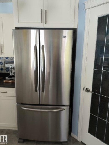 Stainless steel French door refrigerator set within white cabinetry - 59 Rue Monette, Beaumont, AB - Indoor Photo Showing Kitchen