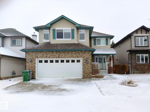 Two-story residence featuring a combination of brick and siding finishes, an attached front-facing two-car garage, multiple upper-level windows with shutters, and a covered front entry - 59 Rue Monette, Beaumont, AB - Outdoor With Facade