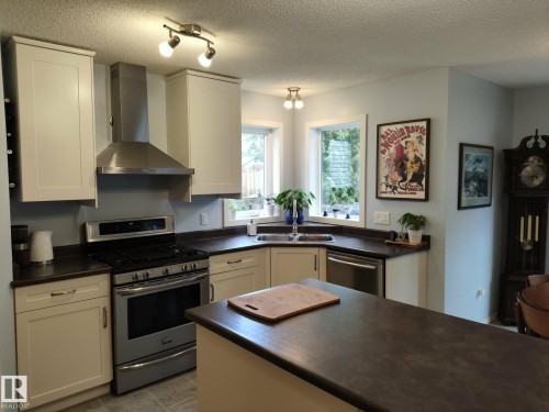 Kitchen featuring white shaker-style cabinetry, stainless steel appliances, dark countertops, and light blue walls - 59 Rue Monette, Beaumont, AB - Indoor Photo Showing Kitchen With Double Sink