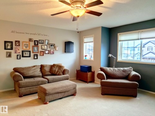 Carpeted room featuring a ceiling fan with integrated lighting, two windows with window treatments, and a wall with contrasting paint - 59 Rue Monette, Beaumont, AB - Indoor Photo Showing Living Room
