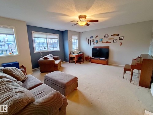 Spacious room featuring multiple windows with white trim, a ceiling fan with integrated lighting, and carpeted flooring - 59 Rue Monette, Beaumont, AB - Indoor Photo Showing Living Room