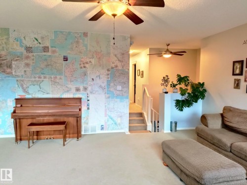 Spacious interior with neutral carpeting and a map-covered accent wall - 59 Rue Monette, Beaumont, AB - Indoor Photo Showing Living Room
