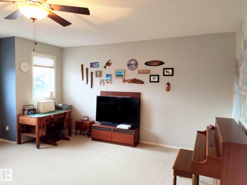 Carpeted room featuring a ceiling fan with integrated lighting, a window with a roller shade, and light-colored walls - 59 Rue Monette, Beaumont, AB - Indoor