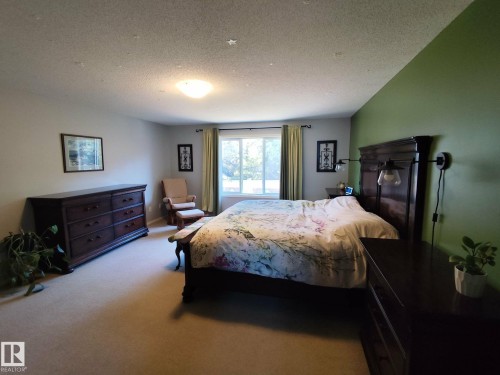 Spacious room featuring neutral carpeting, a large window with drapes, and a vibrant accent wall - 59 Rue Monette, Beaumont, AB - Indoor Photo Showing Bedroom