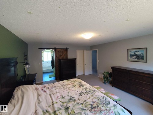 Bedroom featuring neutral wall paint, a textured ceiling, a ceiling-mounted light fixture, and a barn door entry to an additional space - 59 Rue Monette, Beaumont, AB - Indoor Photo Showing Bedroom