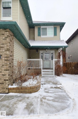 Exterior featuring light-colored siding, contrasting brick accents, a covered front porch with white railings, and a concrete walkway - 59 Rue Monette, Beaumont, AB - Outdoor