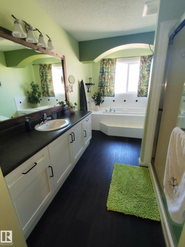 Bathroom featuring a white built-in soaking tub with white tile surround, a spacious vanity with an integrated sink and white cabinetry, wood-finish flooring, and a glass-enclosed shower - 59 Rue Monette, Beaumont, AB - Indoor Photo Showing Bathroom