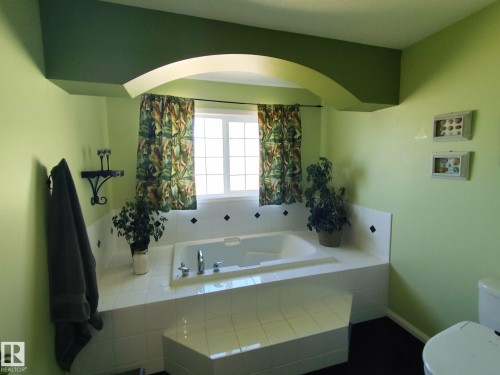 Soaking tub with white tile surround featuring diamond accents, set beneath a large window - 59 Rue Monette, Beaumont, AB - Indoor Photo Showing Bathroom