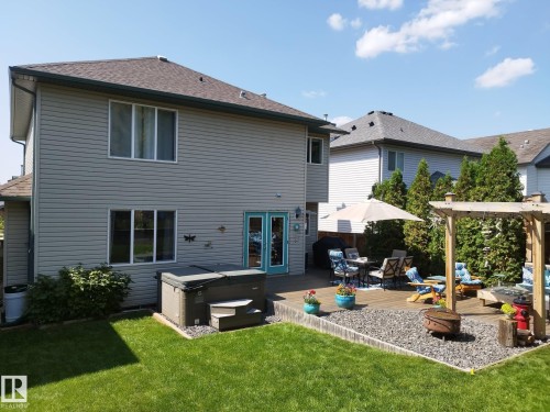 Spacious backyard featuring a large wood-finish deck with built-in pergola, gravel patio area, green lawn, and a hot tub - 59 Rue Monette, Beaumont, AB - Outdoor With Exterior