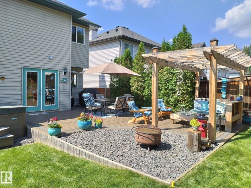 Expansive outdoor deck featuring a wooden pergola, teal french doors, and a decorative gravel fire pit area - 59 Rue Monette, Beaumont, AB - Outdoor With Exterior