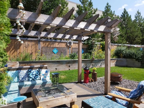 Expansive backyard featuring a wood pergola, a built-in fire pit on a wood-finish deck, a built-in bench with seating, a gravel border, and a raised garden bed with a privacy fence - 59 Rue Monette, Beaumont, AB - Outdoor
