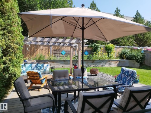 Expansive backyard featuring a wood deck, pergola, privacy fencing, manicured lawn, and mature plantings - 59 Rue Monette, Beaumont, AB - Outdoor With Deck Patio Veranda