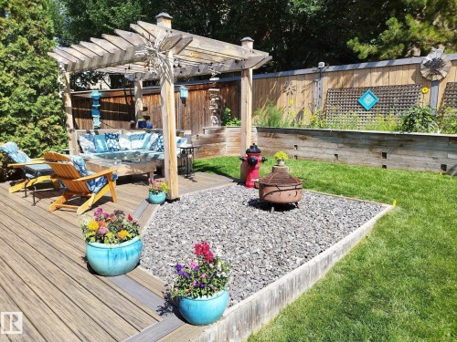 Expansive backyard featuring a multi-level wood-finish deck, a pergola, a gravel fire pit area, a manicured lawn, and a wooden privacy fence with integrated planter boxes - 59 Rue Monette, Beaumont, AB - Outdoor