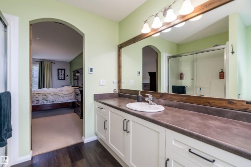 Expansive backyard featuring a multi-level wood deck, a pergola with string lighting, a dedicated gravel fire pit area, a grass lawn, and mature privacy trees - 59 Rue Monette, Beaumont, AB 