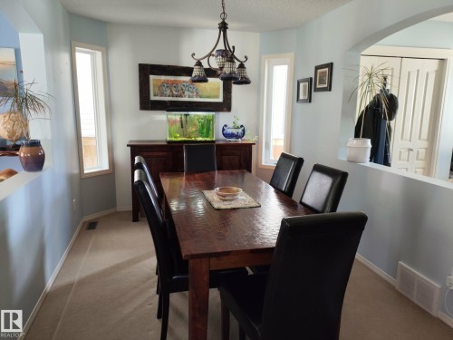 Dining area featuring a central wood-finish table and a decorative chandelier - 59 Rue Monette, Beaumont, AB - Indoor Photo Showing Dining Room