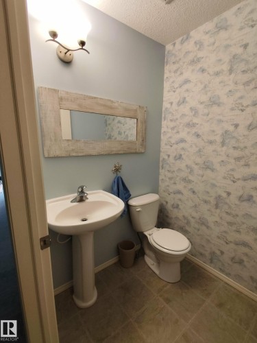 Pedestal sink with chrome faucet, complemented by a distressed wood-frame mirror - 59 Rue Monette, Beaumont, AB - Indoor Photo Showing Bathroom