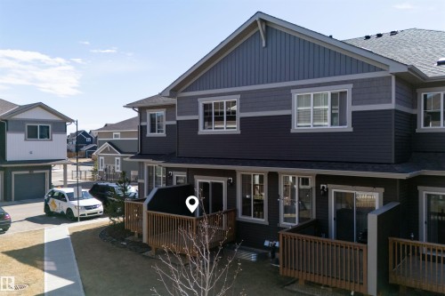 Contemporary townhouse exterior featuring multi-toned siding, white-framed windows, and private ground-level patios with wood railings - 51 603 Orchards Boulevard Sw, Edmonton, AB - Outdoor With Deck Patio Veranda