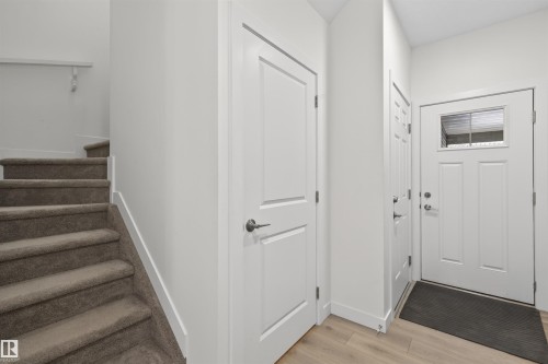 Entryway featuring light wood-finish flooring, white paneled doors, and a staircase with neutral-toned carpeting - 51 603 Orchards Boulevard Sw, Edmonton, AB - Indoor Photo Showing Other Room