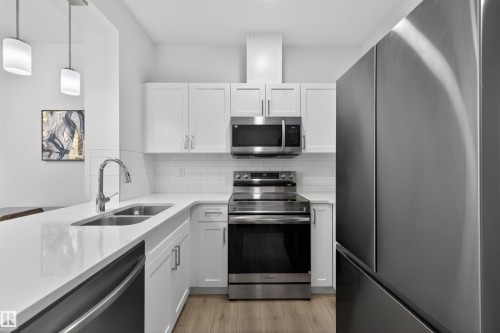 Kitchen featuring white shaker cabinetry, stainless steel appliances, white subway tile backsplash, and light wood-finish flooring - 51 603 Orchards Boulevard Sw, Edmonton, AB - Indoor Photo Showing Kitchen With Stainless Steel Kitchen With Double Sink With Upgraded Kitchen