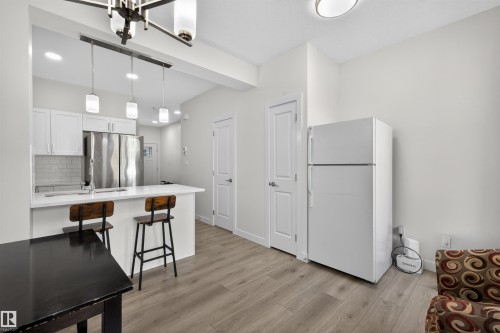 Open-concept kitchen featuring white cabinetry, a white subway tile backsplash, and a breakfast bar with pendant lighting - 51 603 Orchards Boulevard Sw, Edmonton, AB - Indoor Photo Showing Kitchen