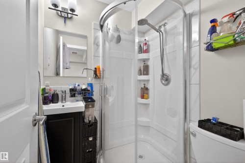 Compact bathroom featuring a glass-enclosed corner shower with built-in shelving, a wall-mounted shower head, and a hand-held sprayer - 51 603 Orchards Boulevard Sw, Edmonton, AB - Indoor Photo Showing Bathroom