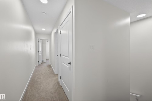 Hallway featuring neutral-toned carpeting, recessed ceiling lighting, crisp white walls, white trim, and interior doors with brushed nickel hardware - 51 603 Orchards Boulevard Sw, Edmonton, AB - Indoor Photo Showing Other Room