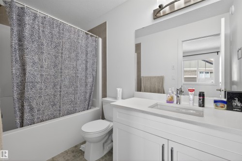 Bathroom featuring a white vanity with integrated rectangular sink, a white bathtub with tile surround, and an overhead light fixture - 51 603 Orchards Boulevard Sw, Edmonton, AB - Indoor Photo Showing Bathroom