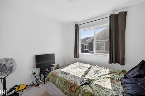 Bright bedroom featuring a large window with dark drapes, white walls, and light-colored carpeting - 51 603 Orchards Boulevard Sw, Edmonton, AB - Indoor Photo Showing Bedroom