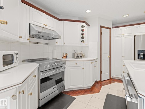 Kitchen featuring stainless steel appliances, decorative backsplash, under cabinet range hood, light tile patterned flooring, and light countertops - 29 Oakdale Place, St. Albert, AB - Indoor Photo Showing Kitchen