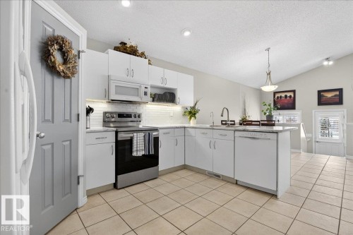 The kitchen features white cabinetry, stainless steel appliances, and a tiled backsplash - 3518 18 Street, Edmonton, AB - Indoor Photo Showing Kitchen
