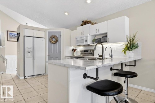 The kitchen features white cabinetry, stainless steel appliances, a white tile backsplash, and a breakfast bar with seating - 3518 18 Street, Edmonton, AB - Indoor Photo Showing Kitchen With Double Sink With Upgraded Kitchen