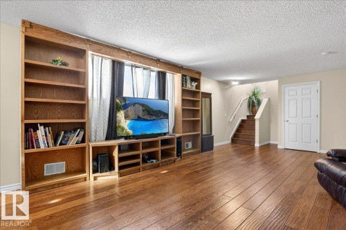Living area featuring hardwood floors, a built-in entertainment unit with shelving, and a stairway with a wooden banister - 3518 18 Street, Edmonton, AB - Indoor