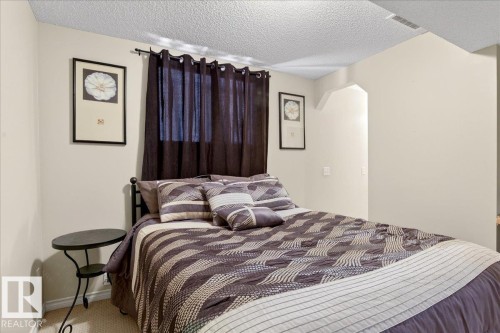This room features neutral-toned walls, a textured ceiling, and a window with dark curtains - 3518 18 Street, Edmonton, AB - Indoor Photo Showing Bedroom