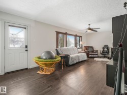Spacious living area featuring wood-finish flooring, white walls, and a textured white ceiling - 