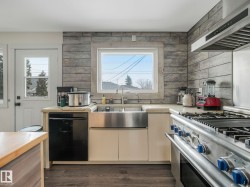Kitchen featuring a stainless steel farmhouse sink, black dishwasher, and a professional-grade range with a coordinating vent hood - 